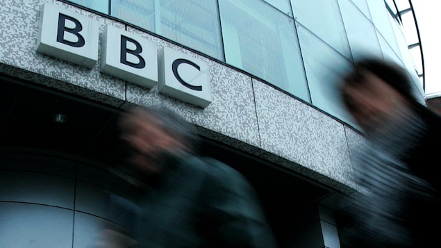 Deux hommes marchent devant les bureaux de la BBC.