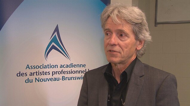 Philippe Beaulieu en entrevue devant une affiche de l'Association.