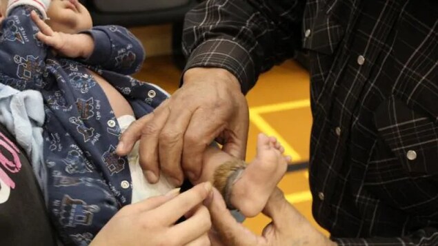 Deux peronnes attachent un bracelet sur la cheville d'un bambin.