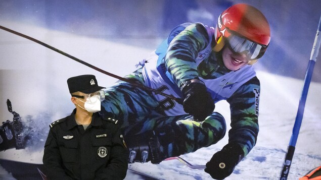 FILE - A police officer wearing a face mask and goggles to protect against COVID-19, stands near a poster of a skier on the wall at a train station in Zhangjiakou in northern China's Hebei Province, Friday, Nov. 26, 2021. China is threatening to take â€œfirm countermeasures" if the U.S. proceeds with a diplomatic boycott of February's Beijing Winter Olympic Games. Foreign Ministry spokesperson Zhao Lijian on Monday accused U.S. politicians of grandstanding over the issue of not sending dignitar