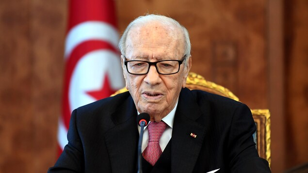 Béji Caïd Essebsi assis devant un micro, le drapeau de la Tunisie derrière lui. Béji Caïd Essebsi assis devant un micro, le drapeau de la Tunisie derrière lui.