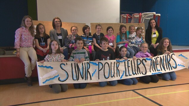 Des jeunes sont assis sur le sol et tiennent une affiche où il est écrit : S'unir pour leurs avenirs. Des jeunes sont assis sur le sol et tiennent une affiche où il est écrit : S'unir pour leurs avenirs.