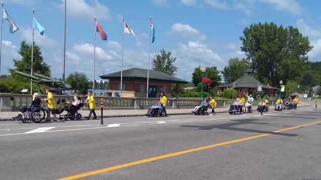 De jeunes bénévoles accompagnent des personnes en fauteuil roulant sur la promenade du Saint-Maurice à Shawinigan.