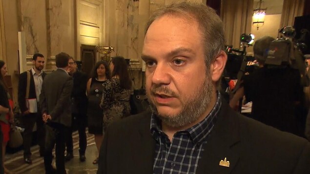 Benoit Dorais, maire de l'arrondissement du Sud-Ouest, en point de presse à l'hôtel de ville, avec un groupe de personnes en train de discuter à l'arrière. Benoit Dorais, maire de l'arrondissement du Sud-Ouest, en point de presse à l'hôtel de ville, avec un groupe de personnes en train de discuter à l'arrière.