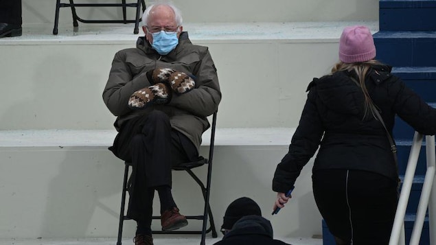 Un vieil homme habillé chaudement, assis sur une chaise pliable et portant un masque.