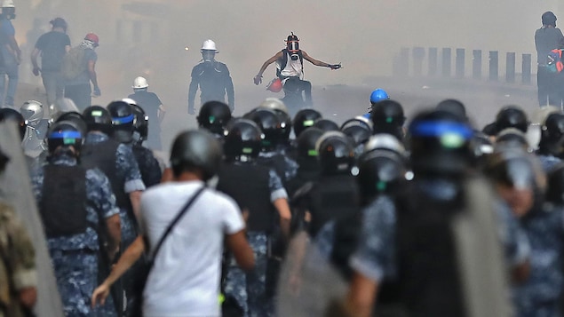 Quelques manifestants portant des masques à gaz défient des policiers en tenu anti-émeute.
