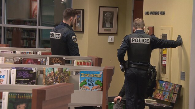 Deux policiers parlent à une personne dans une bibliiothèque.