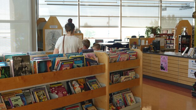 Une femme de dos est dans une bibliothèque avec des enfants. 