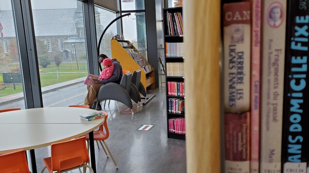 Un père et sa fille assis devant une fenêtre lisent un livre.
