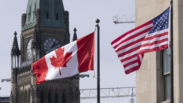 Les drapeaux du Canada et des États-Unis flottent au vent devant la tour de la Paix du Parlement à Ottawa.