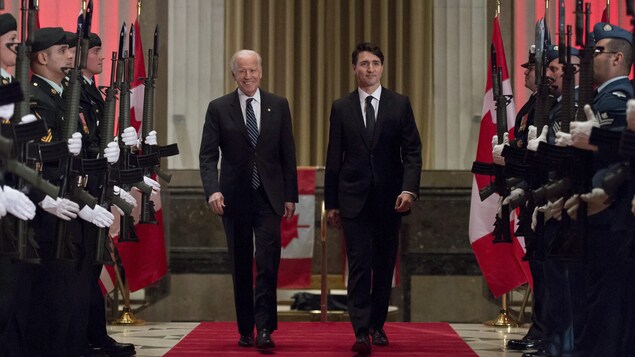 Les deux hommes politiques marchent sur un tapis rouge entre deux rangées de militaires canadiens.