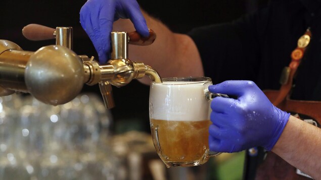 Un serveur ganté verse de la bière en fut dans une pinte.