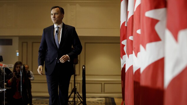 Bill Morneau marche près de drapeaux canadiens.