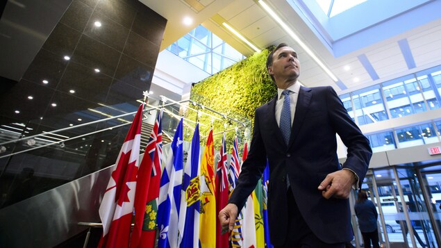 Bill Morneau marche devant les drapeaux du Canada, des provinces et des territoires.