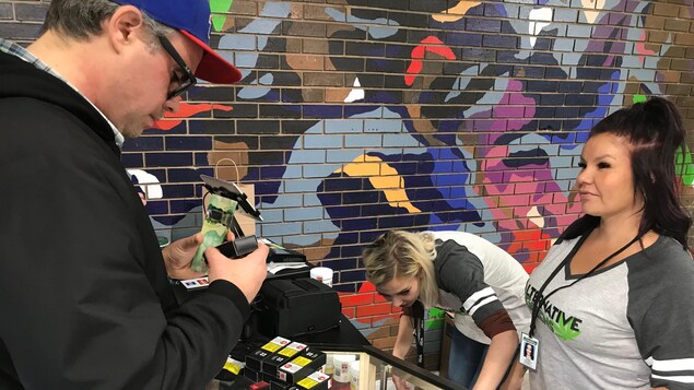 Un client s'apprête à passer à la caisse. Il tient une liasse de billets de 20 $ dans les mains. Un client s'apprête à passer à la caisse. Il tient une liasse de billets de 20 $ dans les mains.