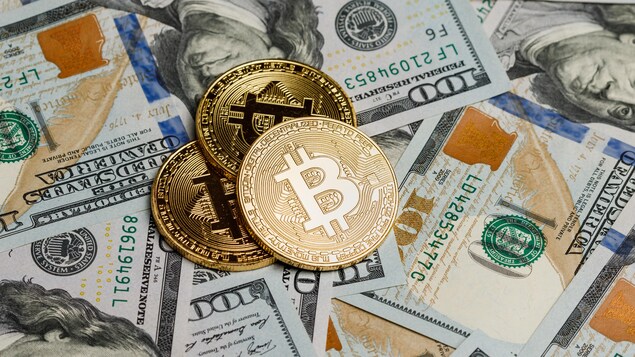Des bitcoins sont déposés sur des billets de 100 $ américains. Des bitcoins sont déposés sur des billets de 100 $ américains.