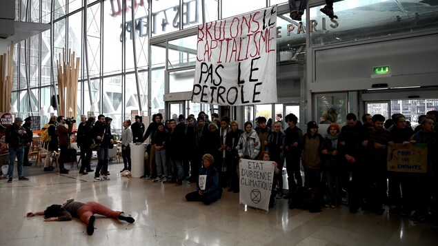 Des dizaines de jeunes se tiennent par le bras sous une banderole où l'on peut lire : « Brûlons le capitalisme, pas le pétrole ».