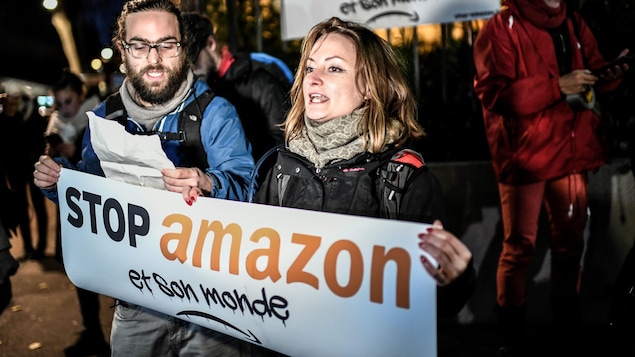 Une femme et un homme tiennent une banderole où il est écrit : « Stop Amazon et son monde ».
