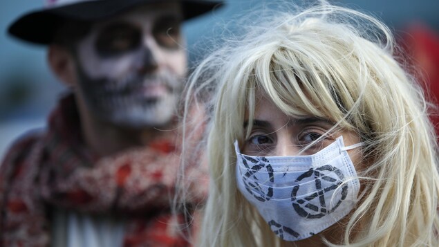 Une femme masquée devant un homme au visage maquillé en tête de mort.