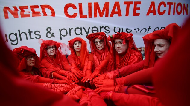 Une dizaine de femmes vêtues de rouge sont placées en cercle et tendent les bras vers le centre dudit cercle.