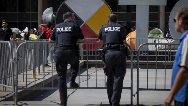 Deux policiers surveillent des manifestants qui campent devant l'hôtel de ville de Toronto.