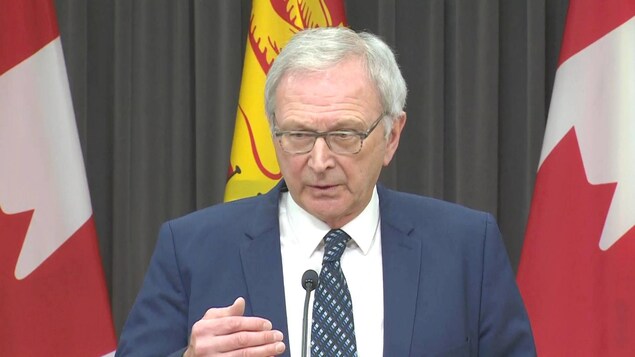 Blaine Higgs devant des drapeaux du Nouveau-Brunswick et du Canada.