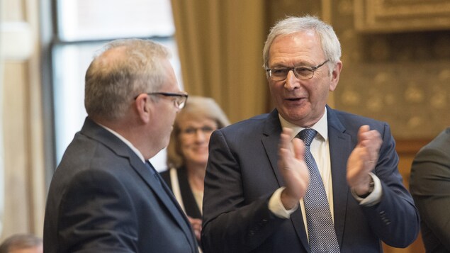 Blaine Higgs est debout. Il sourit et applaudit, tourné vers Ernie Steeves, debout aussi.