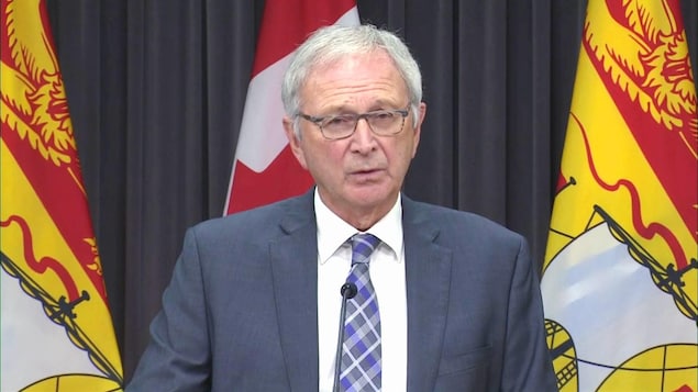 Blaine Higgs en conférence de presse devant des drapeaux du Nouveau-Brunswick.