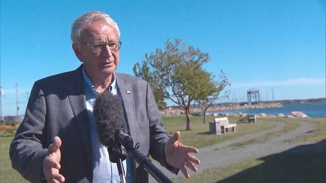 Blaine Higgs donne une entrevue à l'extérieur. On voit le pont au loin derrière lui.