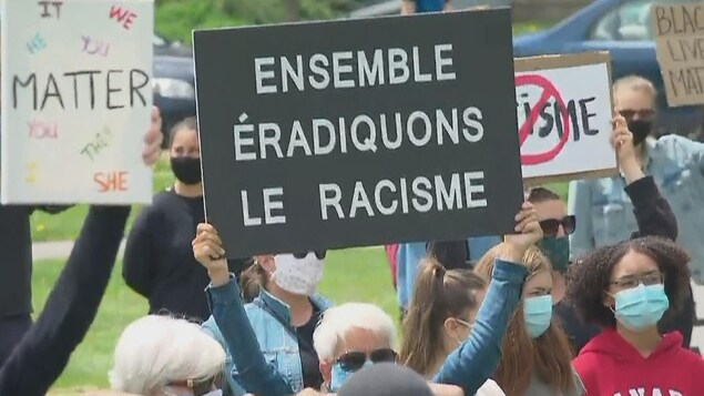 Pendant une manifestation, une personne brandit une affiche sur laquelle est écrit « Ensemble éradiquons le racisme ».