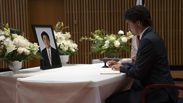 Justin Trudeau signe un livre devant le portrait de Shinzo Abe. 