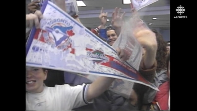 A young boy holds a Toronto Blue Jays flag in a cheering crowd.