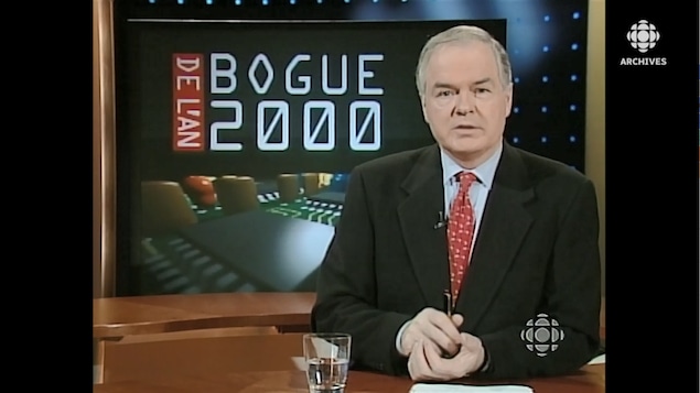 Le présentateur Daniel Lessard à son pupitre de lecteur de nouvelles devant une mortaise annonçant le bogue de l'an 2000