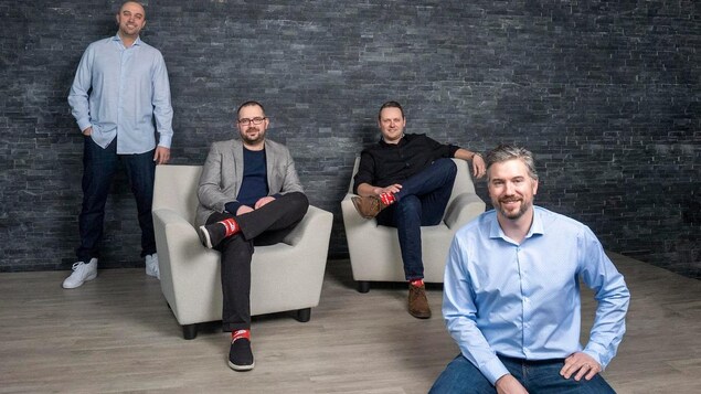 Quatre hommes, dont un debout, deux assis dans des fauteuils et l'un assis au premier plan.