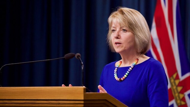 Bonnie Henry, en conférence de presse, devant un drapeau provincial.