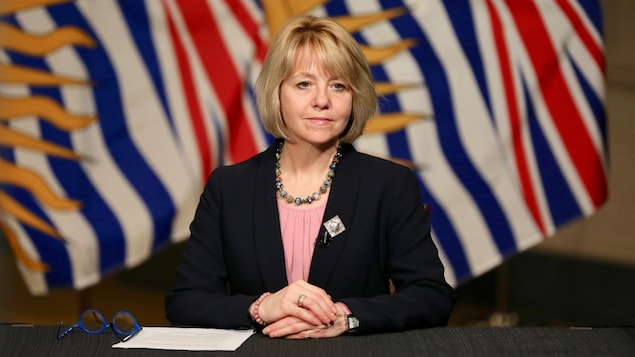 Bonnie Henry en conférence de presse, devant le drapeau de la Colombie-Britannique.