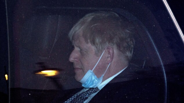 Le premier ministre Boris Johnson portant son masque sous le menton.