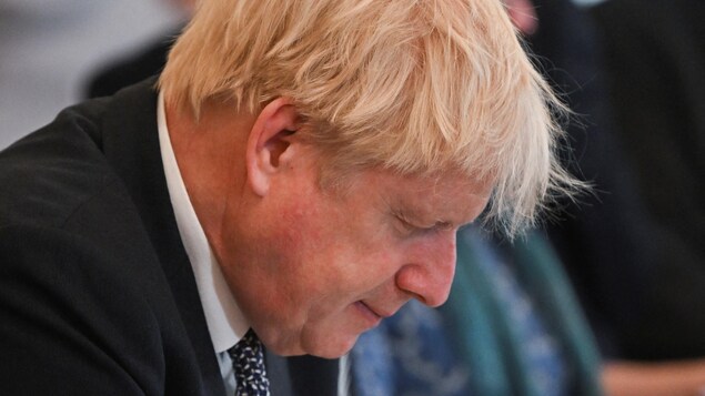 Boris Johnson est assis, la tête baissée, et regarde des documents dans un cartable.