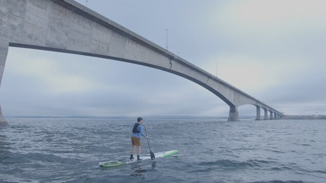 Le jeune homme debout sur sa planche longe le pont de la Confédération.