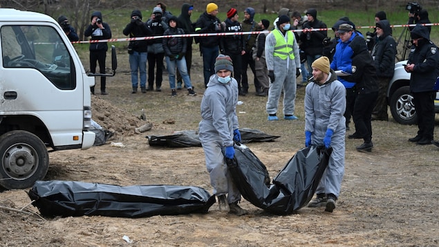 Des journalistes se rassemblent autour de deux hommes qui transportent un sac mortuaire. 