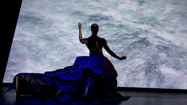 La danseuse est devant un écran vêtue d'une robe en taffetas bleue.