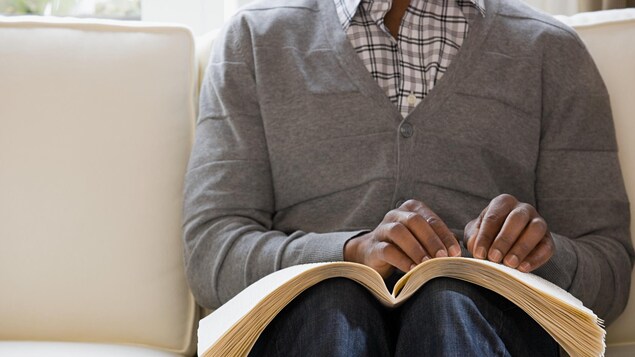 Un homme aveugle lit un livre écrit en braille.