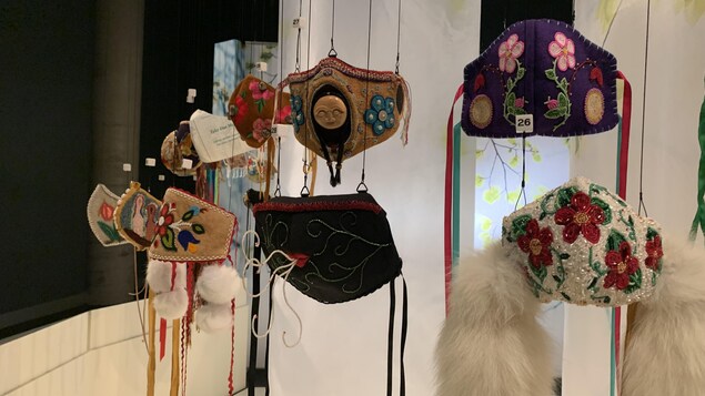 Des masques tissés, perlés et brodés, suspendus dans un musée.