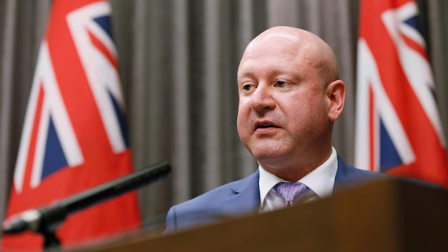 Brent Roussin devant deux drapeaux du Manitoba.
