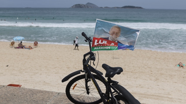 Un drapeau aux couleurs de Lula da Silva flotte sur un vélo garé sur une plage.