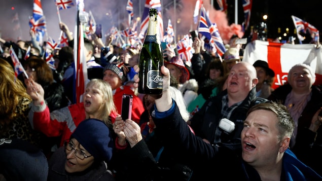 La foule chante et un homme lève une bouteille de champagne.