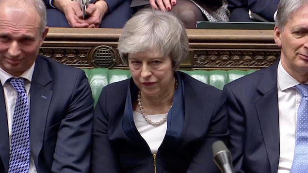 Theresa May, l'air défait, est assise au Parlement.