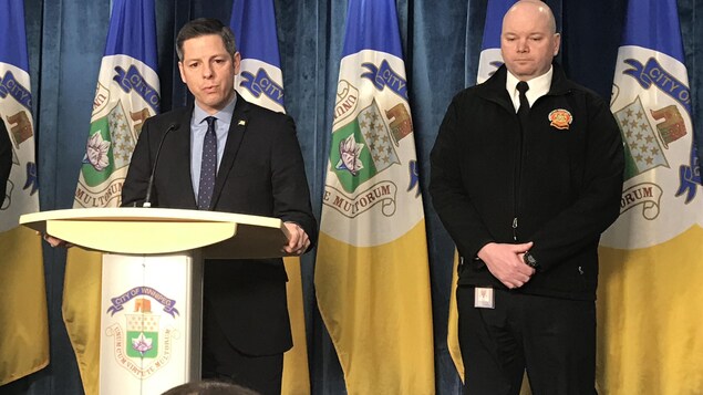 Deux hommes devant des drapeaux de la Ville de Winnipeg.