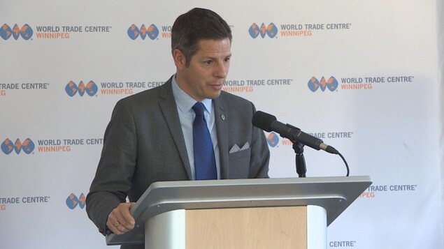 Brian Bowman debout derrière un lutrin avec un micro. Derrière lui, une bannière avec le logo du centre des congrès de Winnipeg. Brian Bowman debout derrière un lutrin avec un micro. Derrière lui, une bannière avec le logo du centre des congrès de Winnipeg.