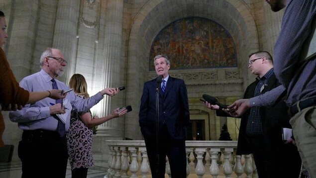 Brian Pallister, entouré de journalistes lors d'une mêlée de presse.